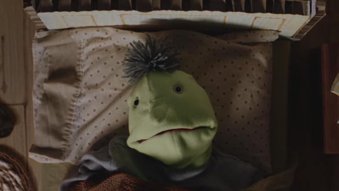 photo of a puppet laying on it's bed whilst looking directly at the camera.