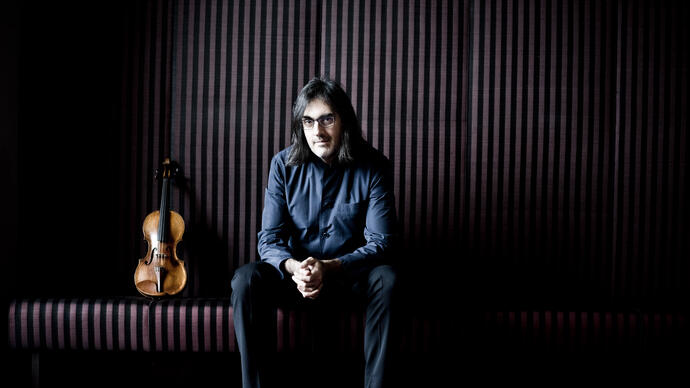 Leonidas Kavakos with his hands clasped sitting on a bench, his violin standing upright next to him