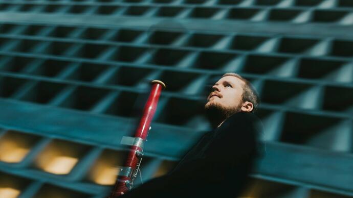 Mathis Stier holding his bassoon in front of a concrete building