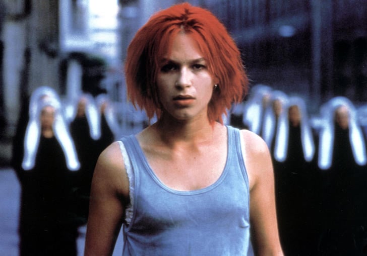 Franka Potente has bright red hair and a grey tank top, standing in front of some blurry nuns in Run Lola Run