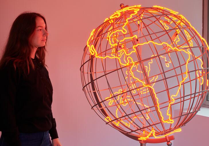 A woman looks at a sculpture of a globe, the outlines of the countries lit in neon orange strip lights.