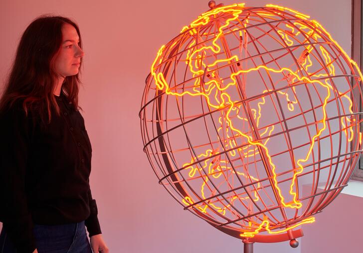 A woman looks at a sculpture of a globe, the outlines of the countries lit in neon orange strip lights.