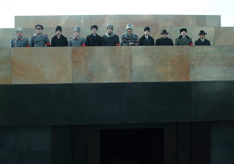 Stalin's peers stand on a concrete balcony dressed in military uniform