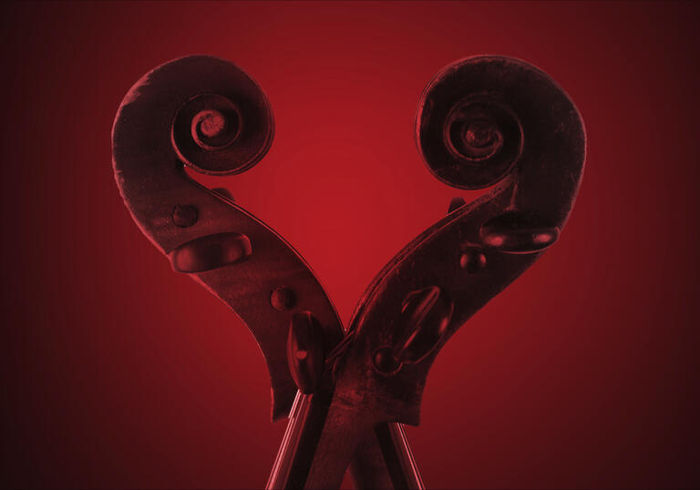 The scrolls of two violins next to each other, forming a love-heart shape. There is a red wash over the image.