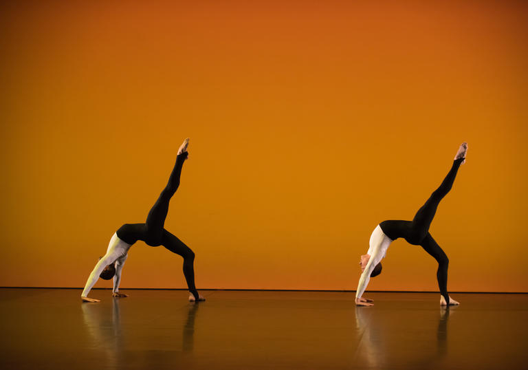 A photo of two dancers from the Michael Clark Company against an orange background.