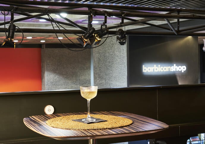 A sake martini cocktail on a high table looking over the foyers and Barbican shop.