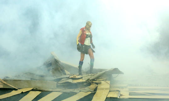 French artist Phia Ménard, who plays Athena stands atop a destroyed cardboard structure surrounded by smoke. Photo by Jean-Luc Beaujault