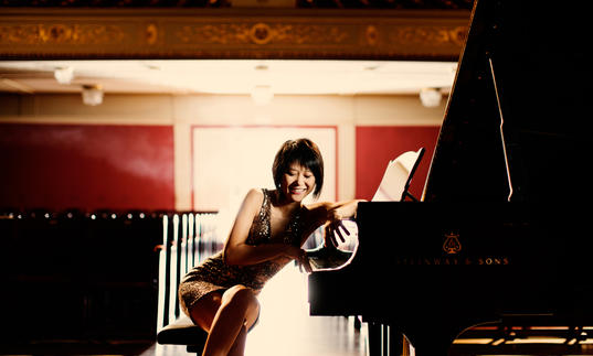 An playful image of Yuja sitting at her piano, facing the camera 