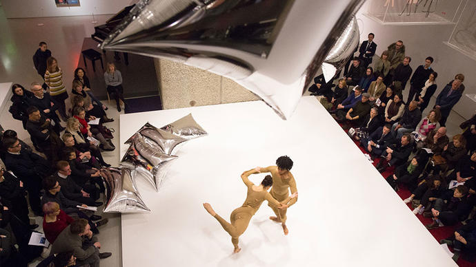 Two dancers perform with silver balloons in an art gallery