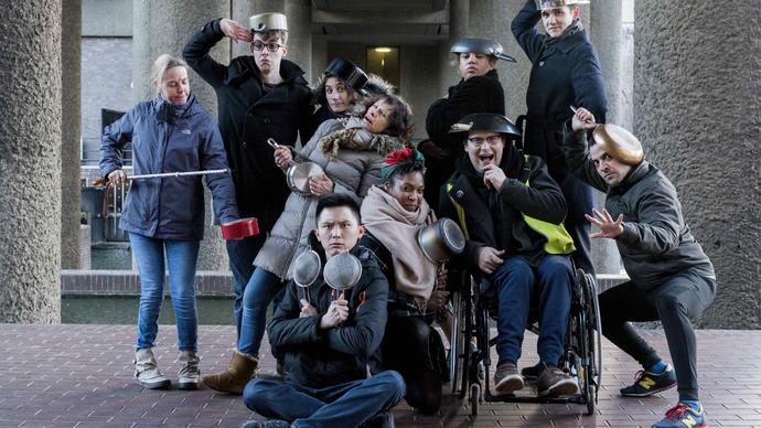 A group photo of the actors from Told By An Idiot standing together doing funny poses with pots and pans on their heads