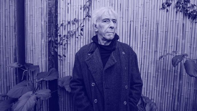 Photo  of John Cale standing in front of a bamboo wall
