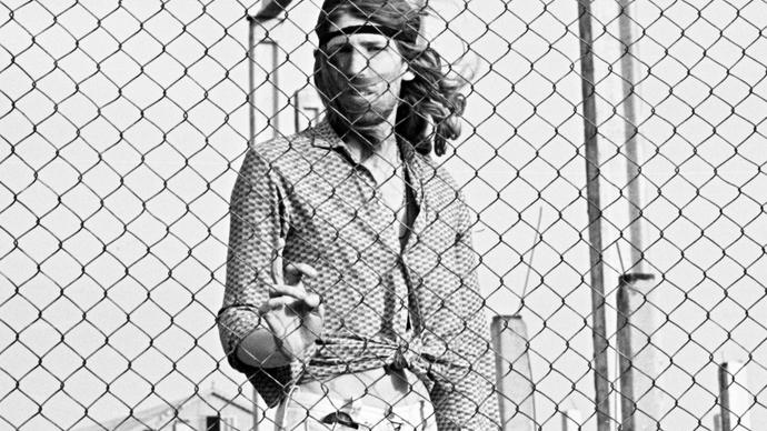 Photo of man with long hair behind a fence