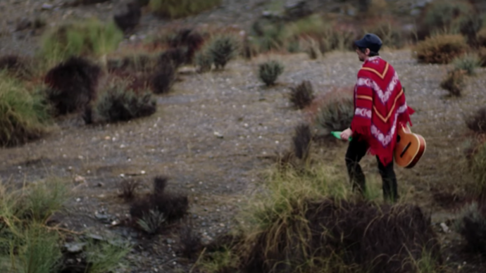 gruff rhys in the desert wearing a red poncho