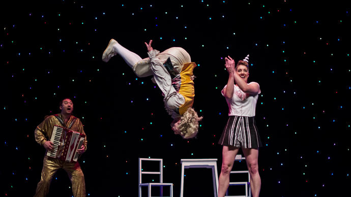 3 people on stage, one doing a flip