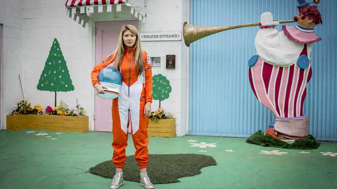 Beatie Wolfe wearing an orange space suit and holding a helmet