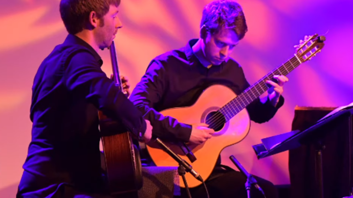 Photo of two men sitting down playing the guitar