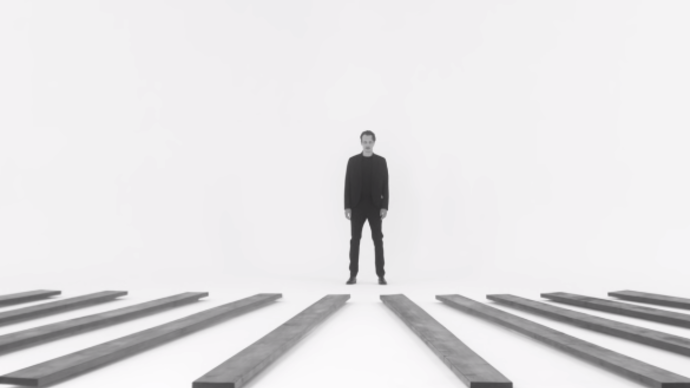 Photo of a man standing in a white room with several planks of wood spaced evenly across the floor
