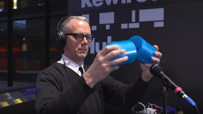 photo of a man with glasses holding a giant blue pill that is open in the middle
