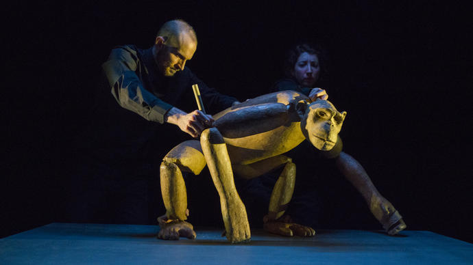 A large chimpanzee puppet is being operated by two of the three puppeteers