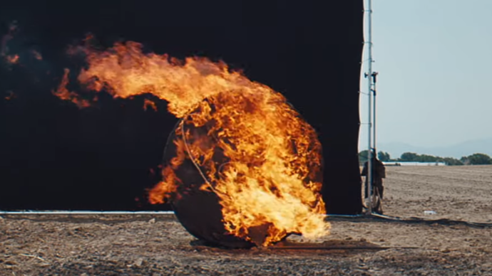 Photo of a black circular object on fire, in the middle of a field 