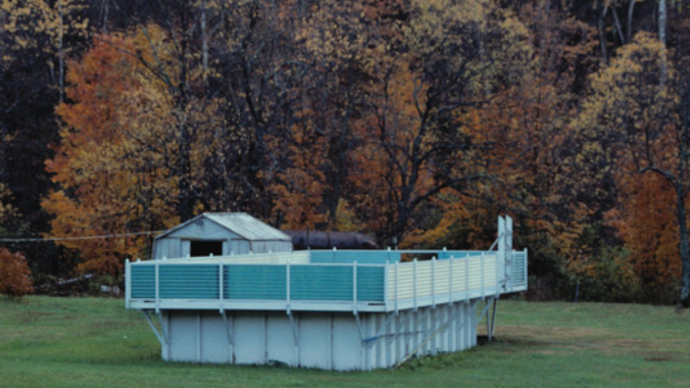 Photo of a house in the middle of a open field with trees in the background