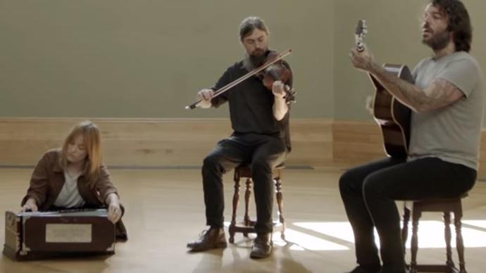 Photo of a girl sitting on the floor, and three men two men sitting on stalls, all playing instruments.