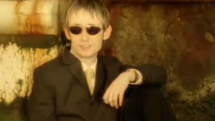 Photo of a man sitting posing towards the camera with black glasses and suit