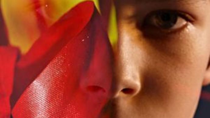 a young child looks at the camera, their face is half covered by yellow and red artwork