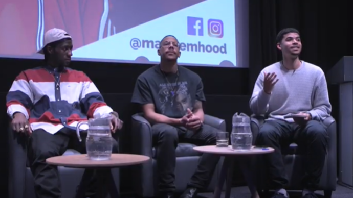 Photo of three men sitting down answering people's questioning at a Q&A