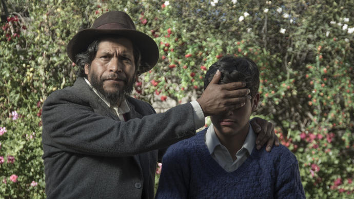 Man in a black suit wearing a hat puts his hand over a boys eyes