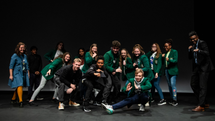 Photo of a large group of teenagers from a school posing for a picture on a stage