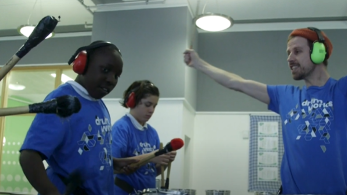 Photo of two boys playing the drums and man cheering them on