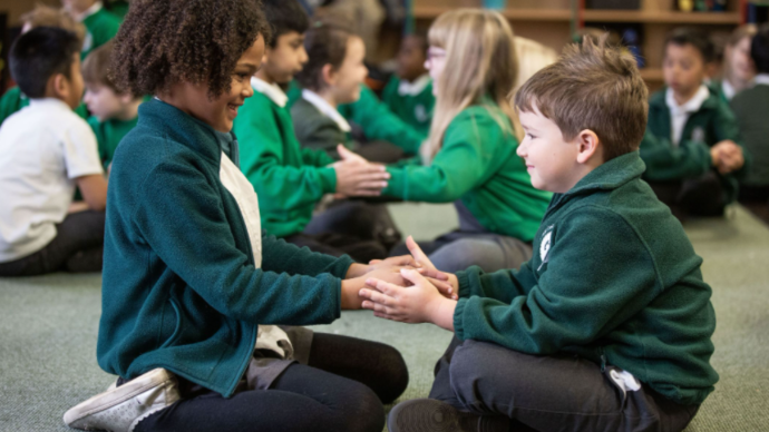 Photo of two school children sitting down facing one another and hold hands