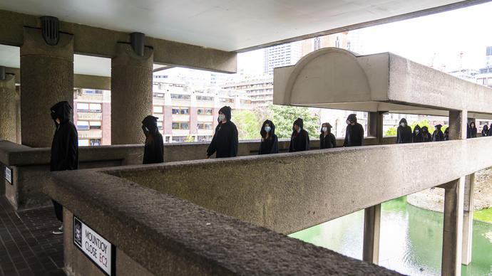 a colour photo of hooded figures wearing all black walking across the Barbican highwalks