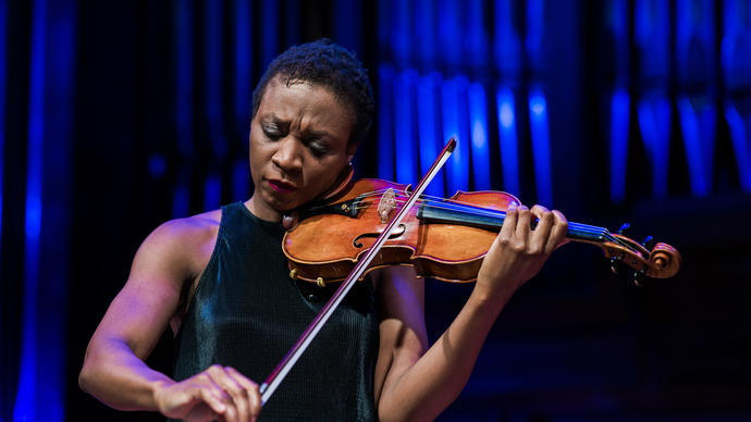 Tai Murray stands playing the violin, in front of organ pipes with a blue light on them