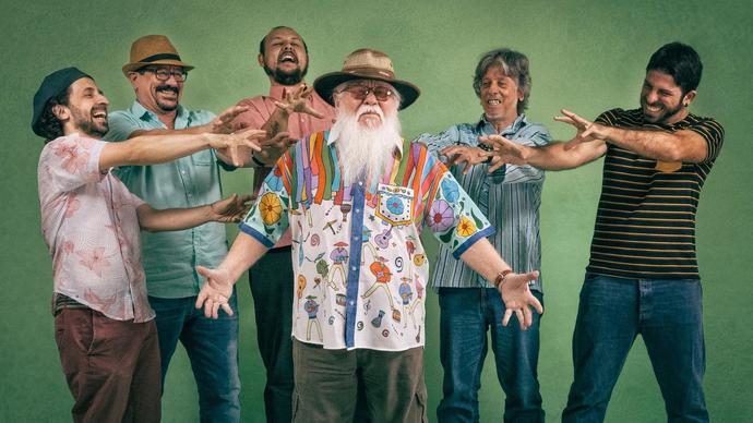Hermeto Pascoal stands wearing a brightly coloured shirt in the centre of the photo while his bandmates point at him