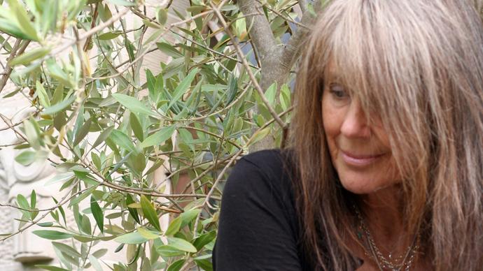 Vashti Bunyan in front of a tree, wearing a black top and long necklaces