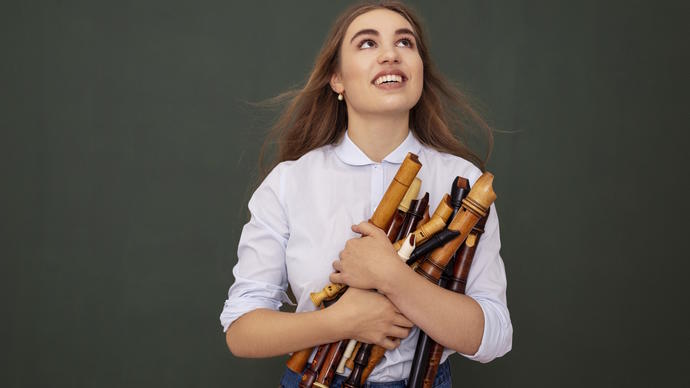 Lucie Horsch stands in the centre of the image, looking up and holding a big bundle of recorders in her arms