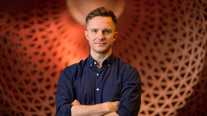 James McVinnie stands in front of a big orange dome, with his arms crossed