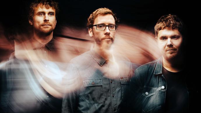 The three members of GoGo Penguin: three white men wearing denim shirts with short haircuts. There is a swirling effect over the image.