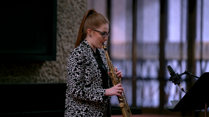 Jess Gillam stands on the Barbican foyer, playing her alto saxophone during a recording session