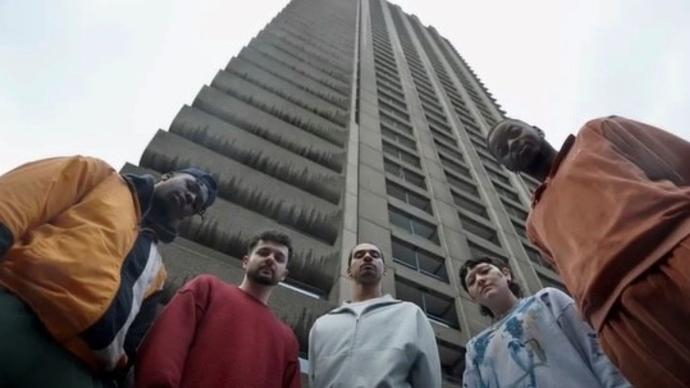 Some of the performers in The PappyShow BOYS pose in front of a high-rise building on the Barbican Estate. They look down at the camera.