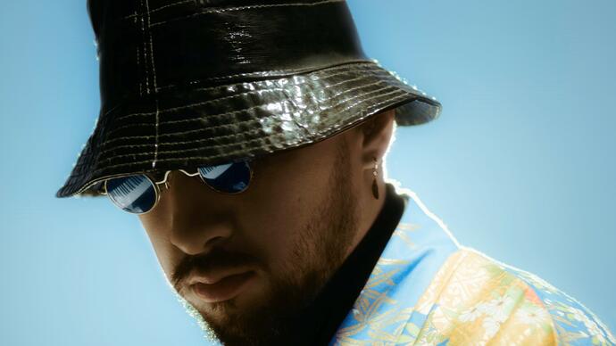 close up photo of Sofiane Pamart against a pale blue backdrop, wearing bucket hat and sunglasses