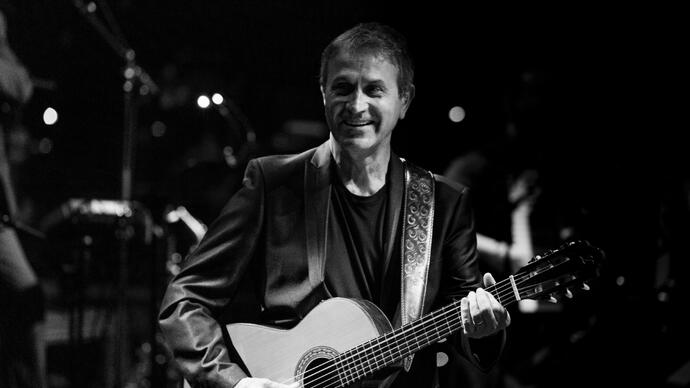 Black and white image of George Dalaras onstage holding a guitar smiling