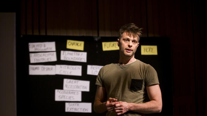 Playwright David Finnigan talks to the audience in front of a board which has notes attached to it.