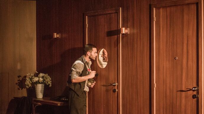 Two performers stare at each other through a circle window in a door.