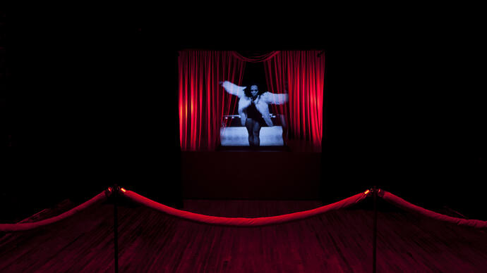 Woman in blue light on the middle of a stage with red curtains on either side