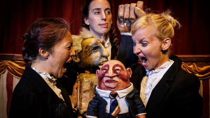 Two puppets and three performers appear to be arguing with each other, one person screams while another looks away cheekily.