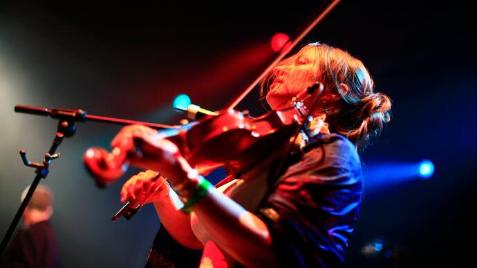 Eliza Carthy playing the fiddle under dynamic lighting on stage