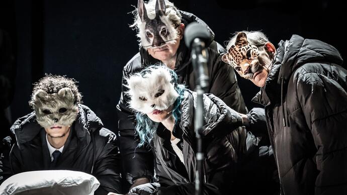 Four people wearing animal masks lean over a table. 